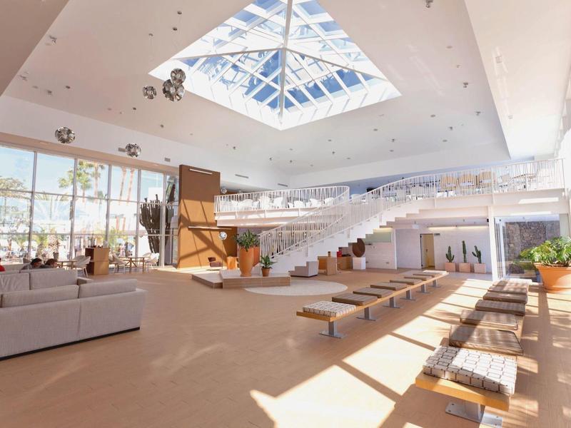 Lobby dell'hotel luminosa e moderna con grande soffitto in vetro e aree salotto.