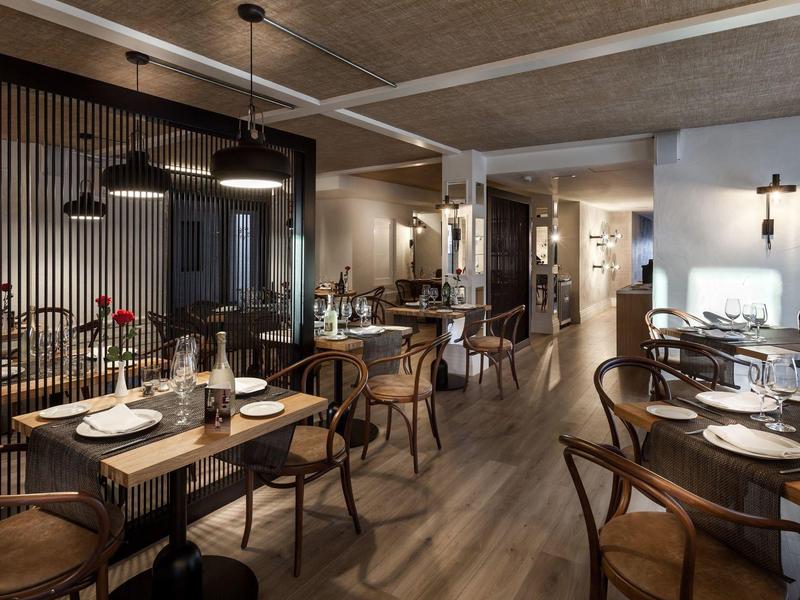 Interno di ristorante moderno con tavoli in legno e sedie eleganti con illuminazione calda.