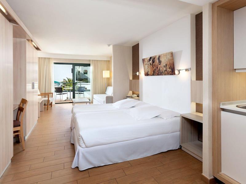 Camera d'hotel moderna con due letti, pavimento in legno e grande finestra con vista sulle palme.