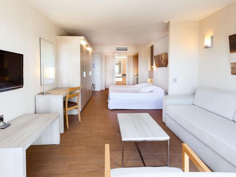 Camera d'hotel luminosa con letto matrimoniale, divano, TV e mobili moderni in legno.