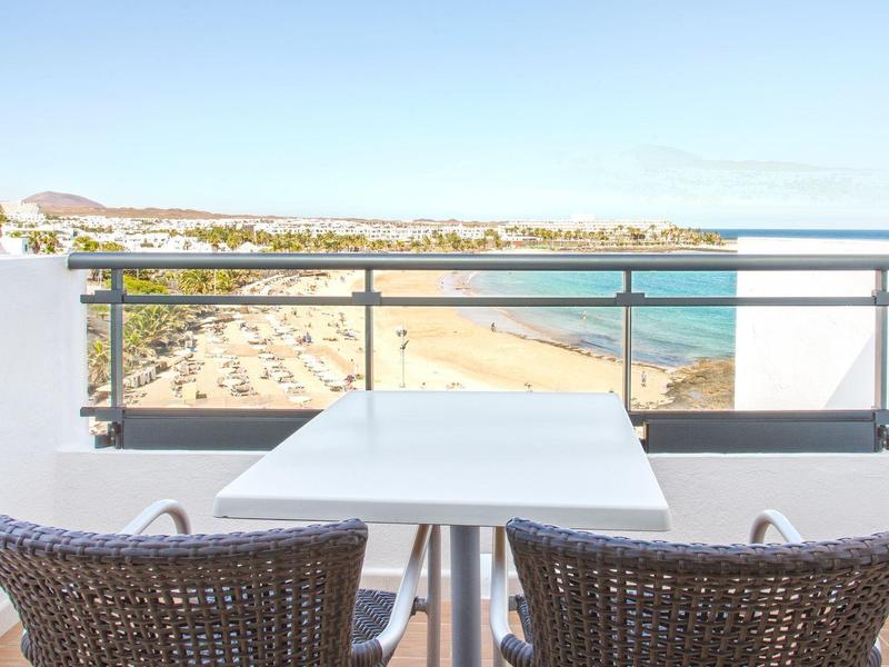 Balcone con due sedie e tavolo con vista sulla spiaggia sabbiosa e il mare.