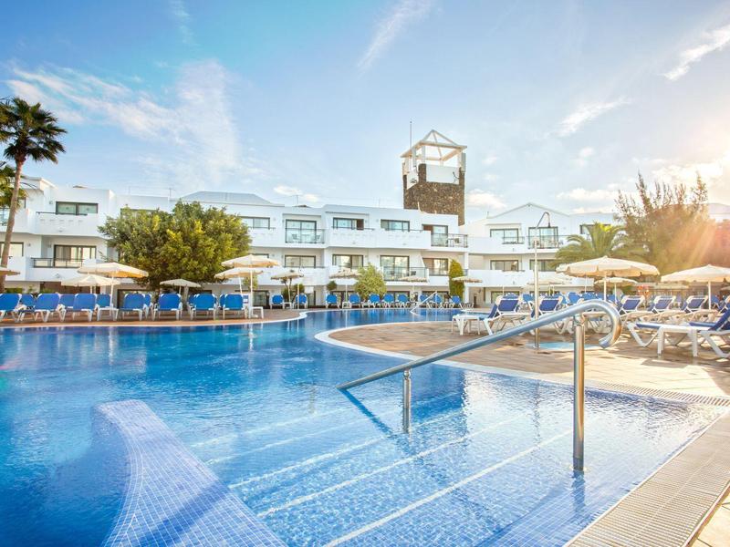Grande piscina all'aperto con sdraio davanti a un moderno edificio dell'hotel al tramonto.