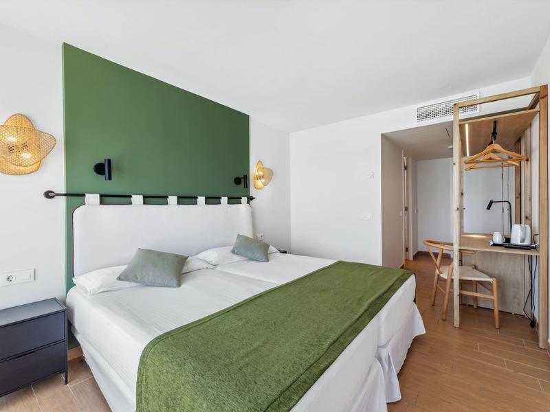 Camera d'albergo moderna con letto matrimoniale, decorazione verde e armadio aperto.