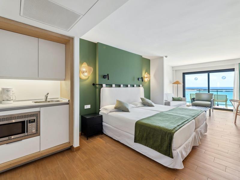 Camera d'hotel moderna con due letti, angolo cottura e balcone con vista mare.