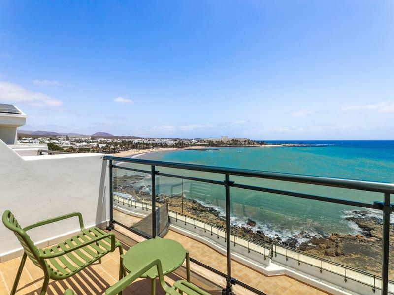 Balcone con sedie verdi e tavolo con vista sul mare e sulla costa.