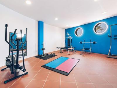 Palestra luminosa con parete blu, tappetini da esercizio e varie attrezzature per il fitness.
