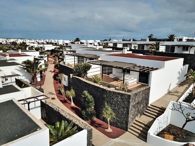 Moderne weiße Häuser mit flachen Dächern, Terrassen und Palmen unter bewölktem Himmel.