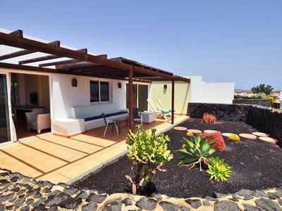 Dom z tarasem, drewnianym stropem i ogrodem z kamieni lawy i roślinami.