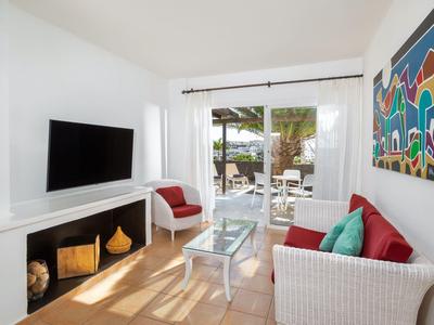 Jasny salon z białą sofą, kominkiem, dużym telewizorem i widokiem na taras przez duże okna.