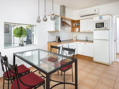 Jasna, nowoczesna kuchnia z stołem jadalnym, białymi szafkami i czerwonymi krzesłami przy dużym oknie.