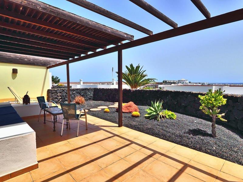 Taras z pergolą, stołem jadalnym, krzesłami i widokiem na ogród i morze.