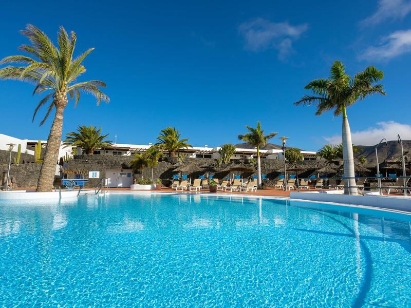 Duży niebieski basen z palmami i leżakami pod czystym niebem w ośrodku.