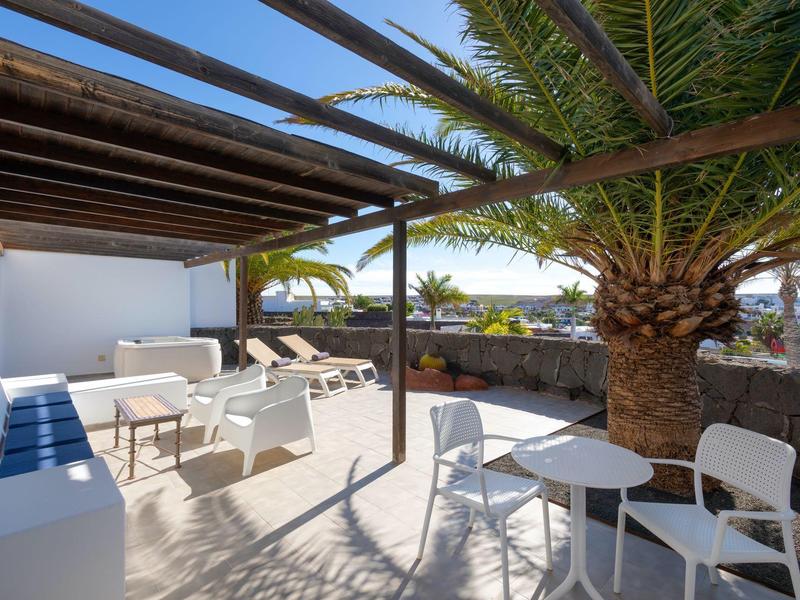 Taras z miejscami do siedzenia, leżakami i palmą, słoneczny i otwarty.