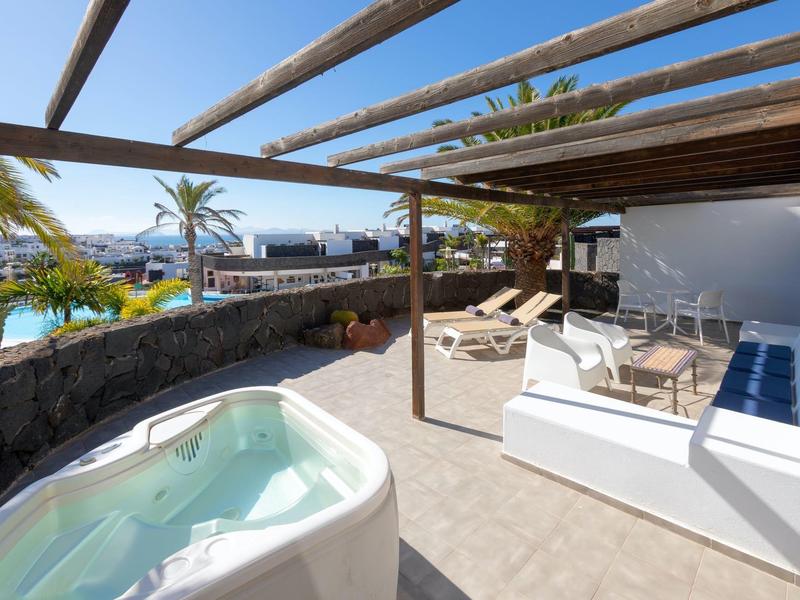 Taras z jacuzzi, strefą wypoczynkową i widokiem na basen pod otwartą drewnianą pergolą.