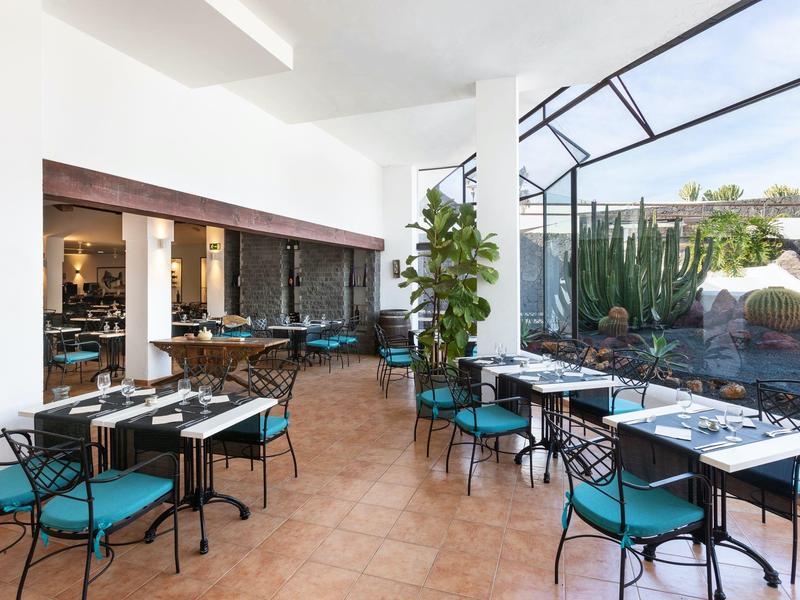 Nowoczesna oranżeria z stołami i krzesłami obok ogrodu z kaktusami.