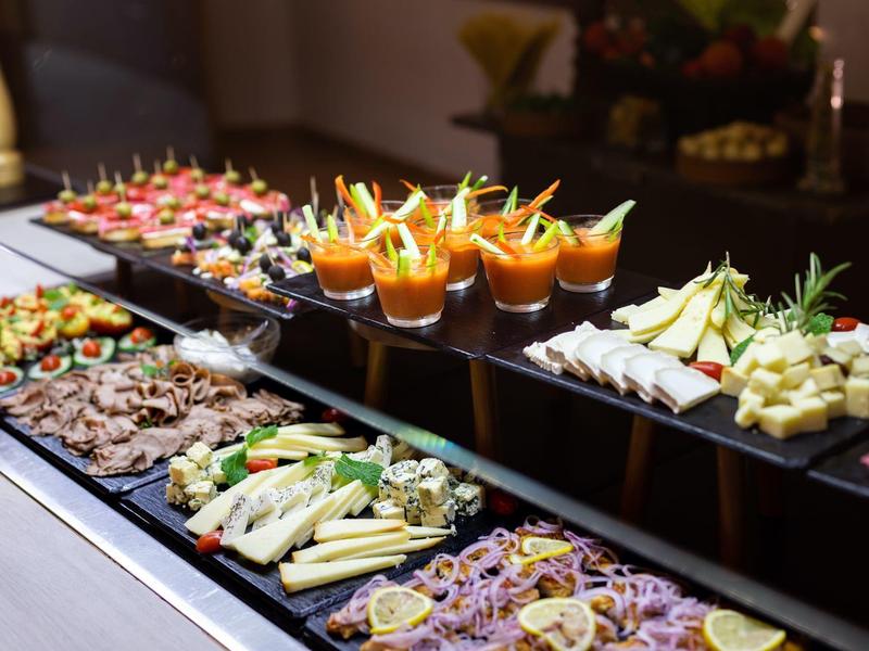 Bufet z różnymi przystawkami, w tym warzywami, mięsem i małymi kieliszkami z dipami.