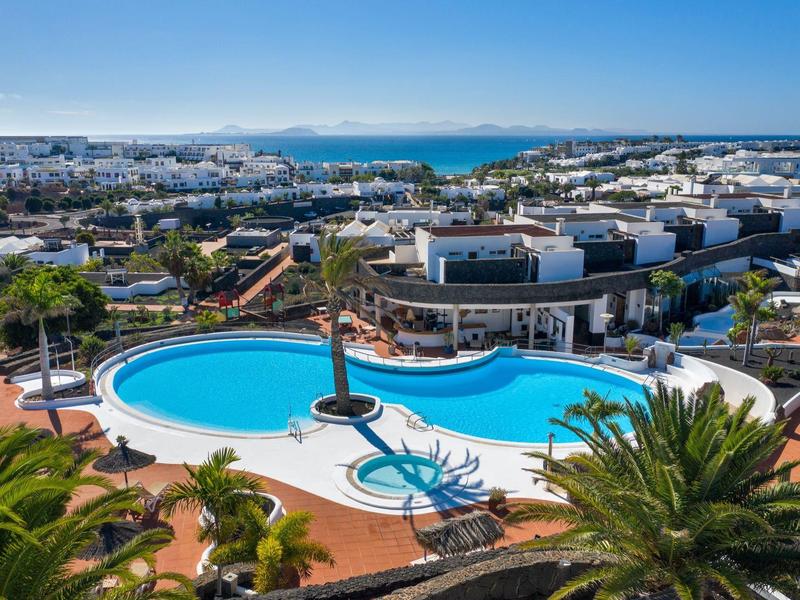 Widok na kompleks hotelowy z krzywym basenem, palmami i morzem w tle.