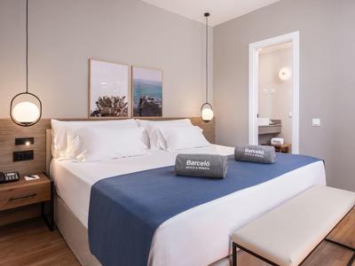 Modern hotel room with large bed, nightstands, lighting, and two pictures on the wall.