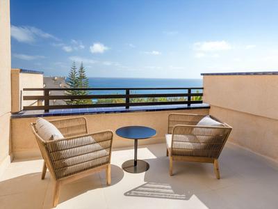 Two garden chairs and a small table on a terrace overlooking the sea.