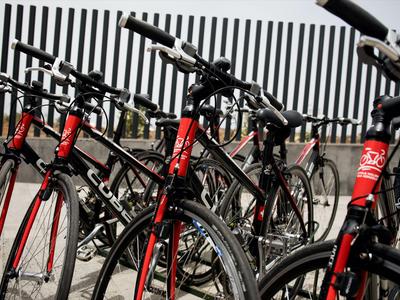 Mehrere rote und schwarze Fahrräder sind geparkt und in einer Reihe vor einem Zaun aus Metallstreben angeordnet.