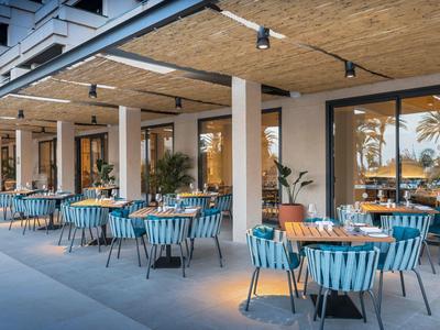 Hotel outdoor seating area with blue chairs and wooden tables under a shaded roof.
