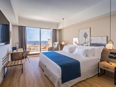 Bright hotel room with double bed, balcony, and sea view.