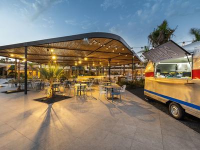 Moderner Außenbereich mit Sitzplätzen und beleuchtetem Food-Truck bei Dämmerung.