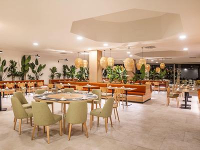 Modern restaurant with plants, green chairs, and wooden tables in a bright setting.