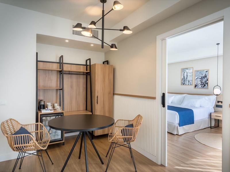 Modern hotel room area with dining space, wardrobe, and view into bedroom.