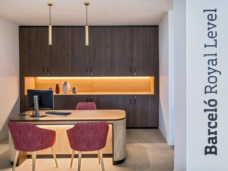 Modern hotel reception with wood paneling, desk, and two red chairs.