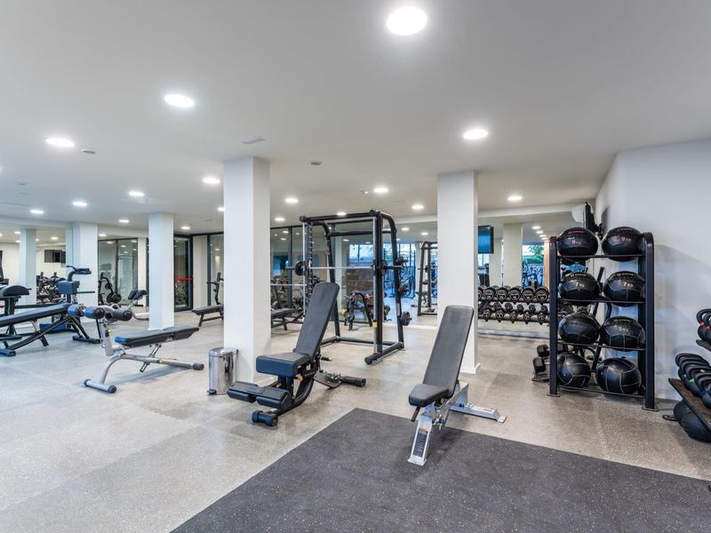 Modern hotel gym with dumbbells, weight machines, and mirrors on the walls.