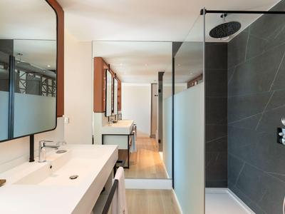 Helles Badezimmer mit großen Spiegeln, Doppelwaschbecken und moderner Dusche mit dunkelgrauen Fliesen.