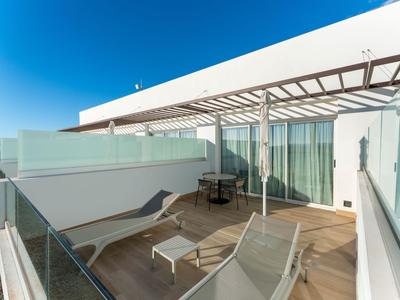 Modernes Hotelbalkon mit Glasgeländer, Sonnenliegen und Tisch unter blauem Himmel.