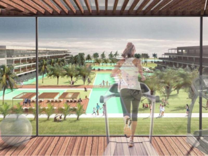 Widok przez szklaną ścianę na luksusowy ogród resortu z basenem, palmami i spacerującymi ludźmi.