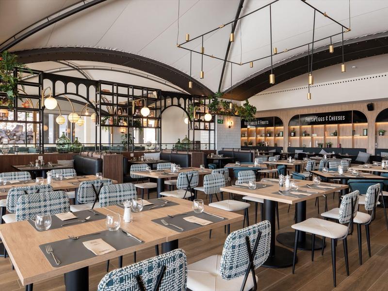 Elegancka restauracja z drewnianymi stołami, wygodnymi krzesłami i nowoczesnym oświetleniem pod białym dachem namiotu.