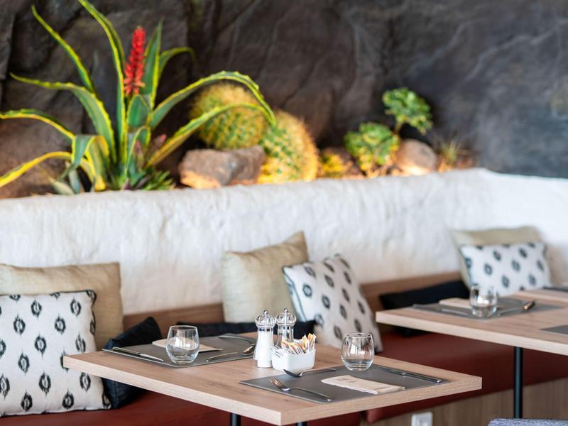 Nowoczesny salon hotelowy z stołami, krzesłami i dekoracyjnym miejscem z roślinami.