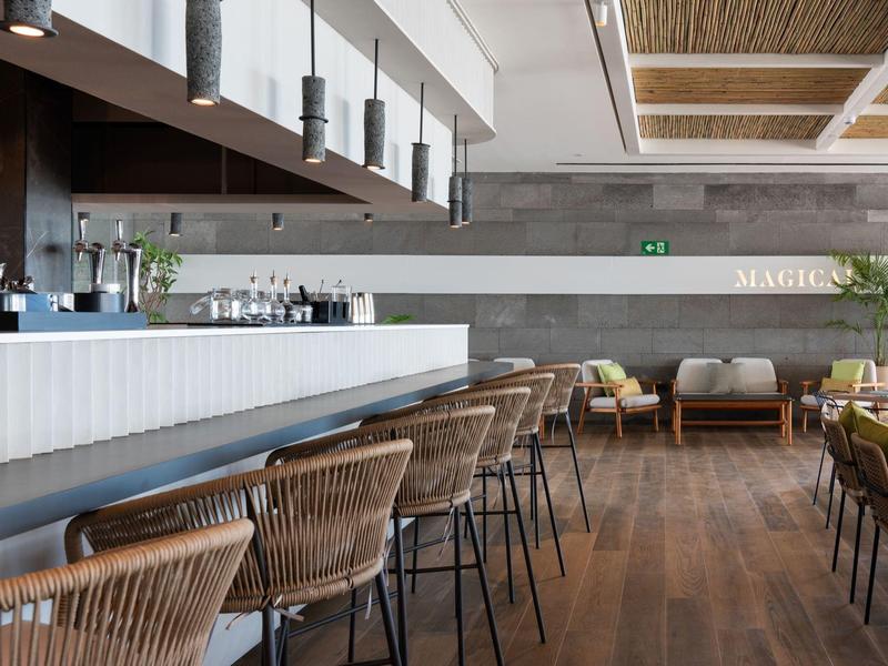 Nowoczesny bar hotelowy z hokerami, drewnianą podłogą i przytulnymi miejscami do siedzenia.