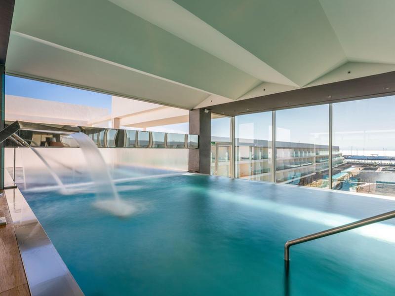 Kryty basen z wodospadem i szerokim widokiem na morze w nowoczesnym hotelu