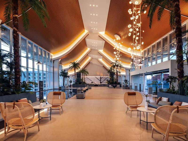 Jasny, nowoczesny hol hotelowy z wysokimi sufitami, skórzanymi fotelami i roślinami.