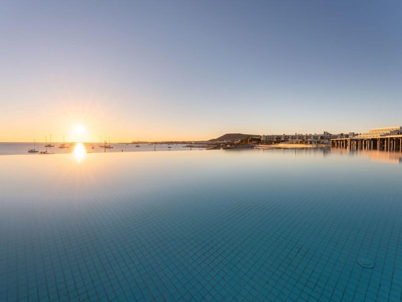 Rozległy basen infinity z widokiem na morze o zachodzie słońca.