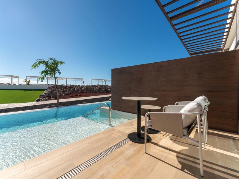 Nowoczesny basen z leżakiem, stolikiem i widokiem na zielony trawnik pod czystym niebem.