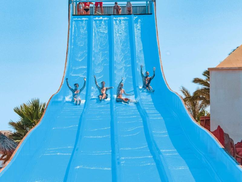 Plusieurs personnes descendent un large toboggan d'eau bleu sous un ciel dégagé.