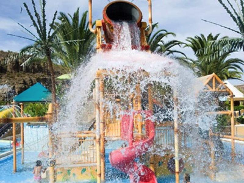 Parc aquatique avec un grand seau basculant et des structures de jeu colorées dans la piscine.