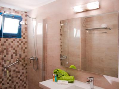 Helles Badezimmer mit großer Wandspiegel, grünem Handtuch, Duschbereich und kleinem Fenster.