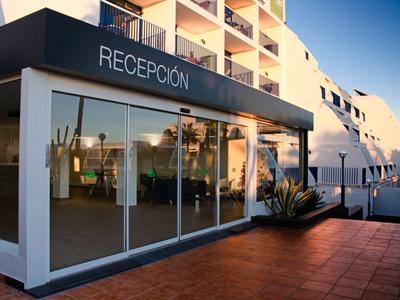 Moderner Empfangsbereich mit Glasfront und Pflanzen, angrenzend an mehrstöckiges weißes Gebäude.