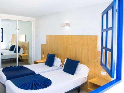 Een lichte hotelkamer met twee eenpersoonsbedden, blauwe kussens en een spiegel tegenover.