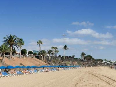 Breiter Strand mit blauem Himmel, Palmen und vielen blauen Sonnenliegen am Meerufer.