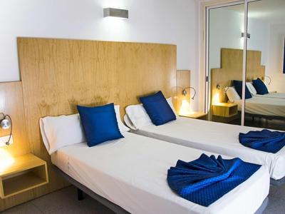 Zwei Einzelbetten mit blauen Kissen und Decken, Holz-Kopfteil und Spiegel-Schrank im Zimmer.