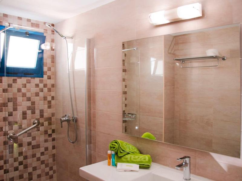 Helles Badezimmer mit großer Wandspiegel, grünem Handtuch, Duschbereich und kleinem Fenster.