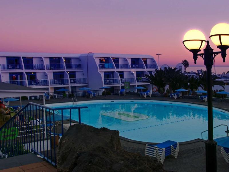 Moderner Hotelpool bei Sonnenuntergang mit beleuchteten Laternen und blauen Liegestühlen.